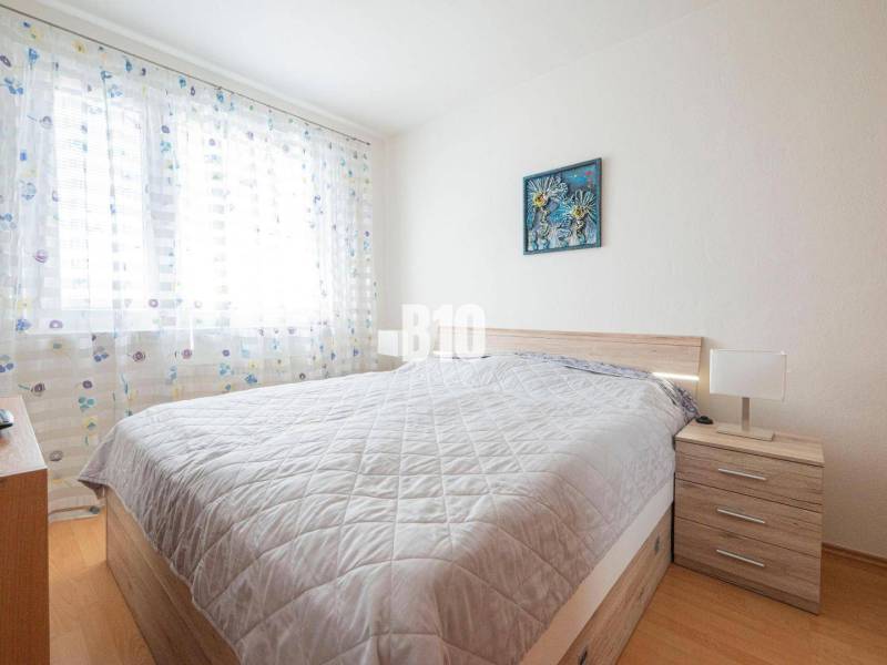 Bedroom in a 3-room apartment with a double bed, a painting, and a nightstand.
