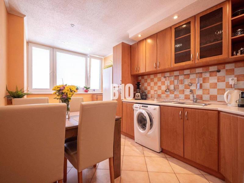 A kitchen in a 3-room apartment with a wooden cabinet, dining table, and washing machine.