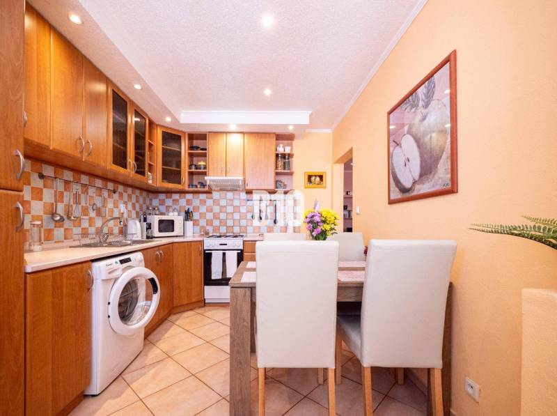 A kitchen in a 3-room apartment with wooden cabinets, a dining table, and a washing machine.