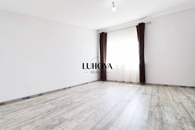 An empty room with white walls, brown curtains, and a wooden floor in a family house.