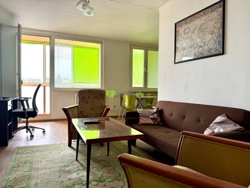 Living room in a three-room apartment with a brown couch, armchairs, and a desk.