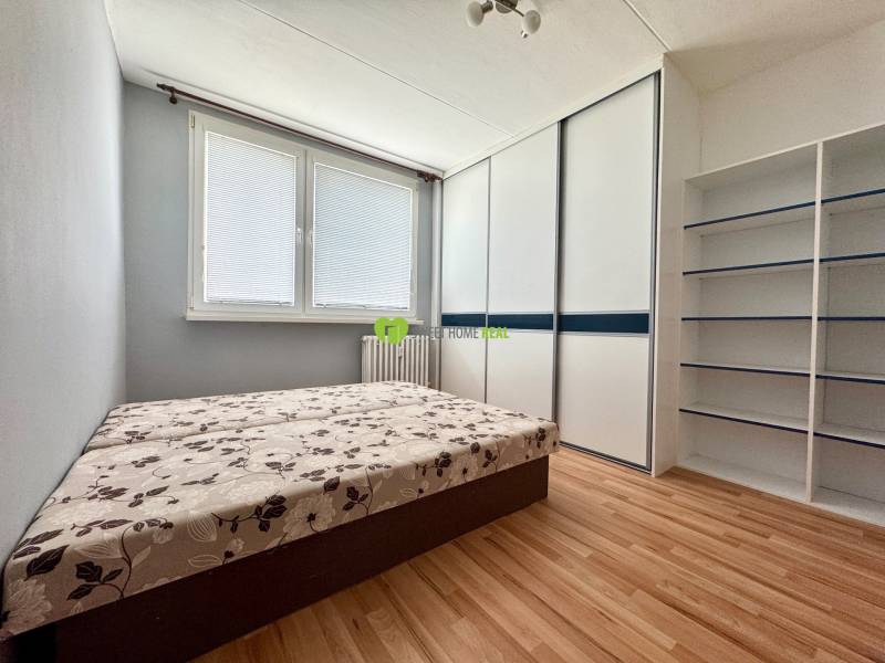 A room in a 3-room apartment with a bed, wardrobe, and shelves on the wall.