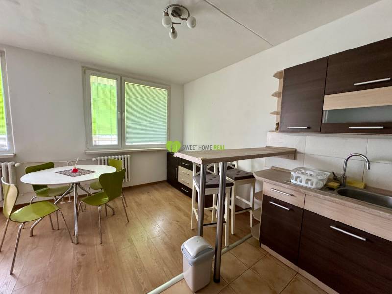 A kitchen in a 3-room apartment with a round table, green chairs, and a kitchen unit.