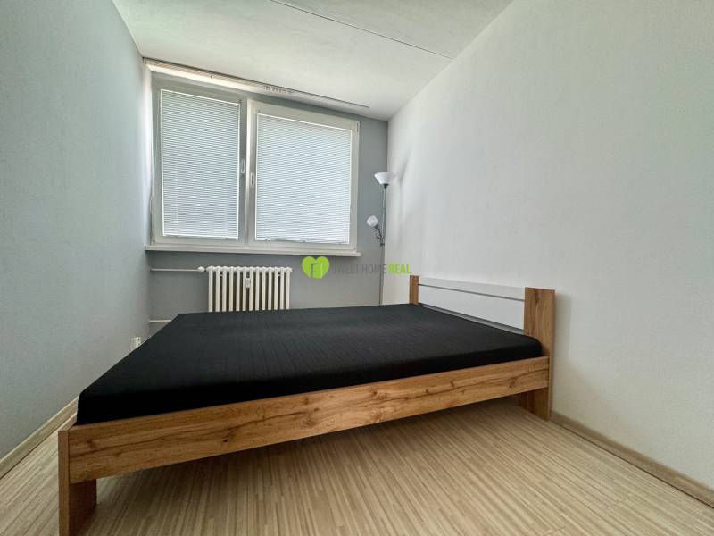 A simply furnished bedroom with a bed and a lamp in a 3-room apartment.