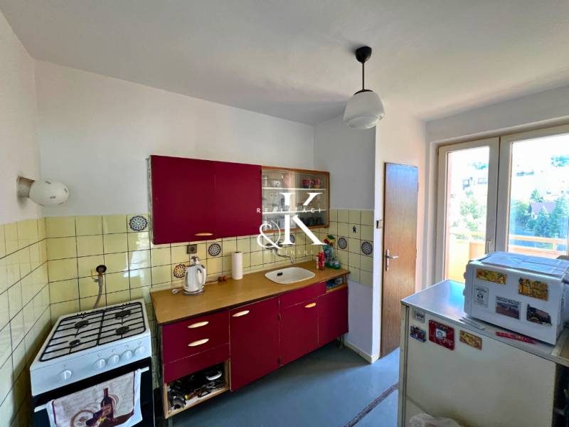The kitchen of a two-room apartment with red cabinets and an older gas stove.