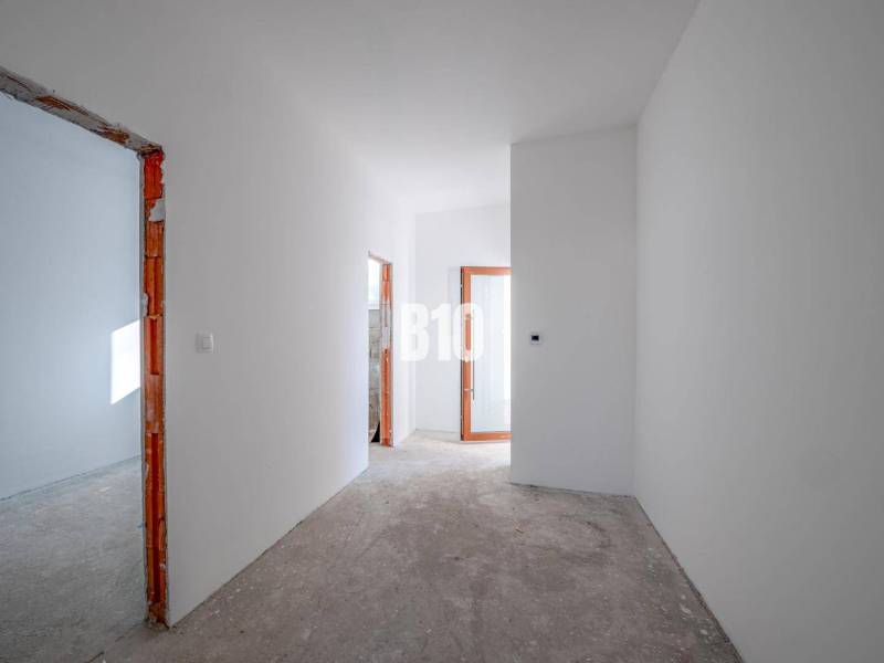 A hallway in a family house with white walls and an unfinished floor.