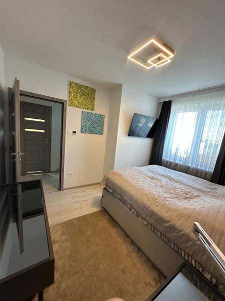 Bedroom in a family house with light, television, paintings, and a large window.