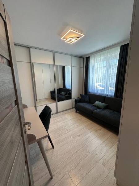 A room in a family house with a black couch, a desk, and a mirrored wardrobe.