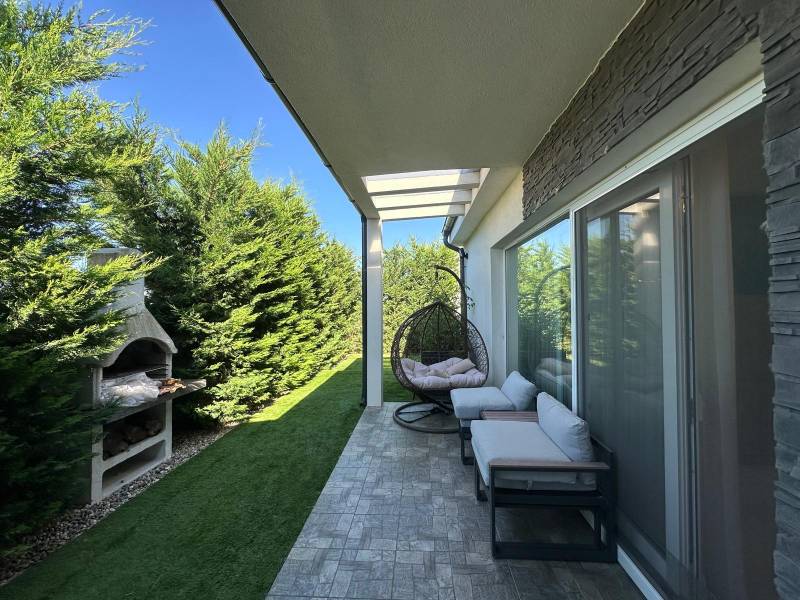 The terrace of a family house in Gabčíkovo with comfortable seating, a swing, and a fireplace.
