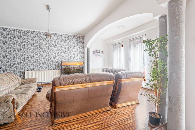 Living room with a leather sofa, patterned wallpaper, and a plant in a family house.