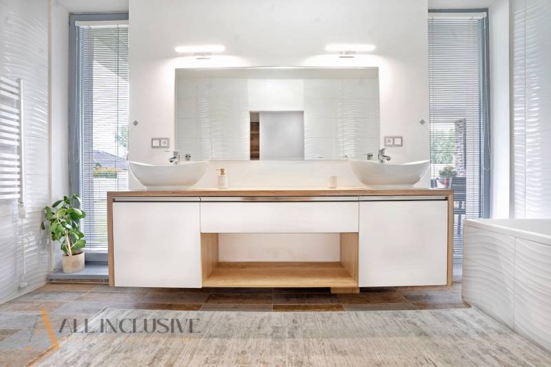 A bathroom in a family house with two sinks, a large mirror, and a decorative plant.