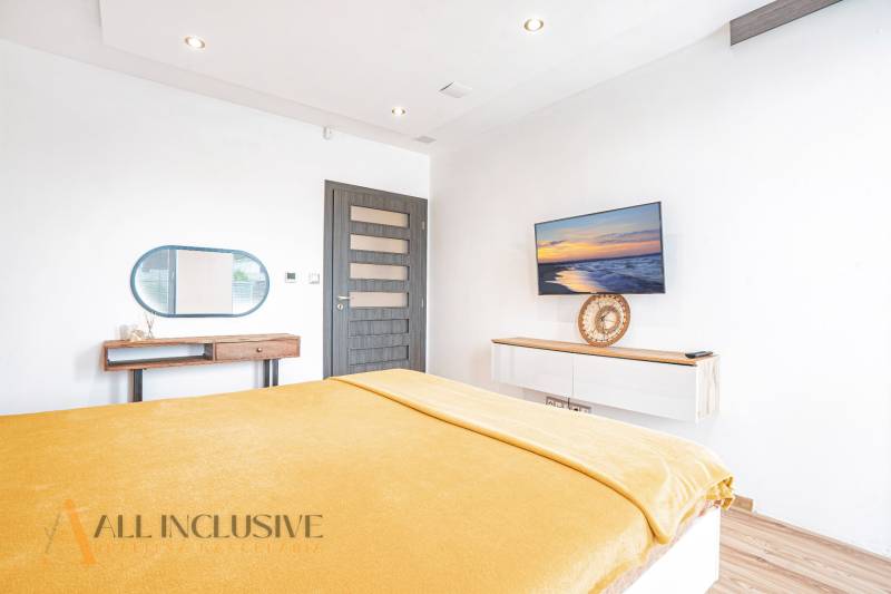 Bright bedroom in a family house with a TV, mirror, and yellow blanket on the bed.
