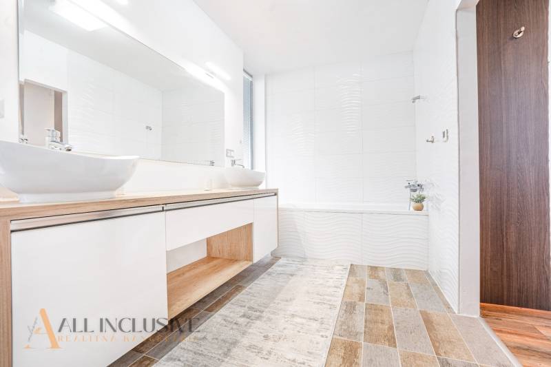 A bathroom in a family house with sinks, white walls, and wooden flooring.