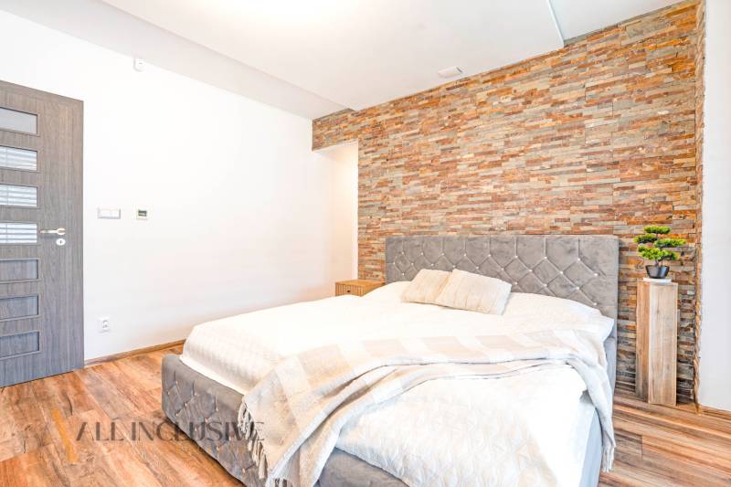 A bedroom in a family house with a stone wall, an elegant bed, and decorative accessories.