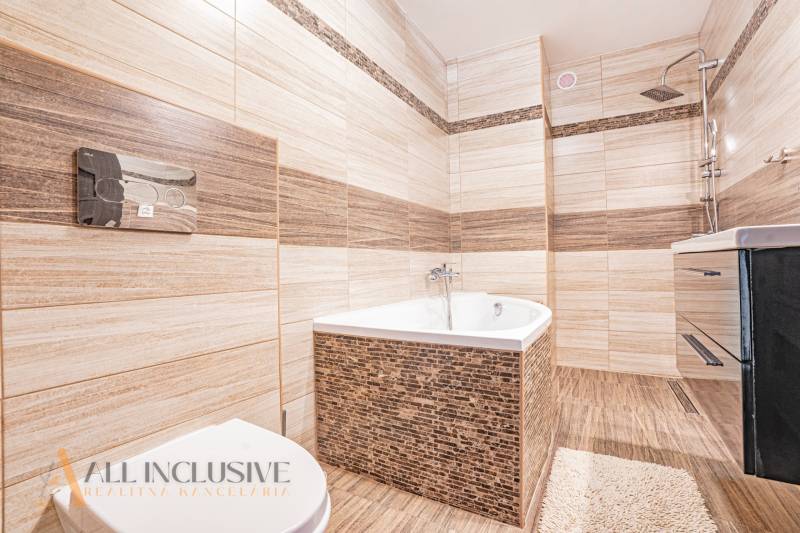 A bathroom in a family house with a bathtub, shower, and sink, surrounded by beige tiles.