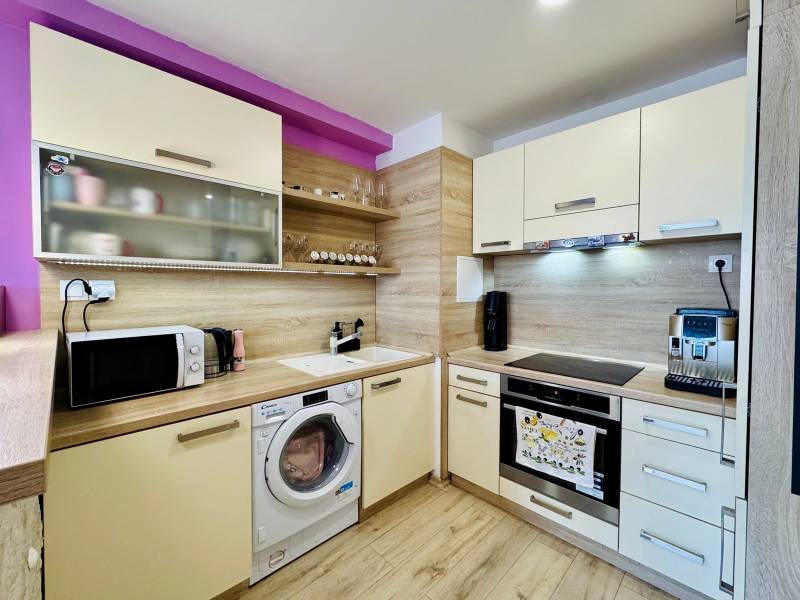 A kitchen in a 2-room apartment with white cabinets, wooden decor, and appliances.