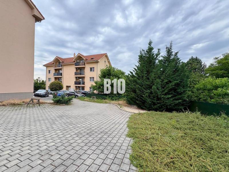 An apartment building in Nitra with three floors surrounded by greenery and a parking lot.