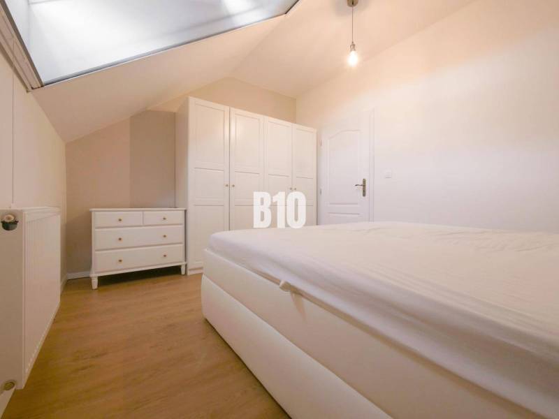 A bedroom in a 3-room apartment with a slanted ceiling, a white bed, and a wardrobe.