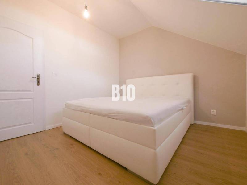 A bedroom in a 3-room apartment with a white bed and wooden flooring.
