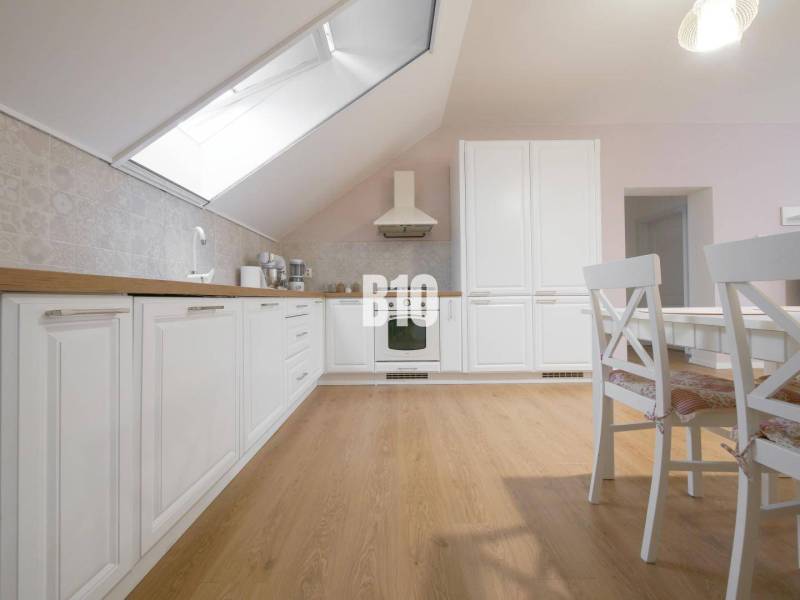 A bright kitchen in a 3-room apartment with white cabinets, wooden flooring, and a dining table.