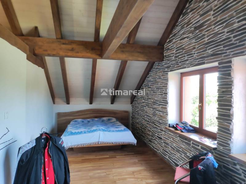 Attic bedroom with wooden beams, stone cladding, and a bed in a 2-room apartment.