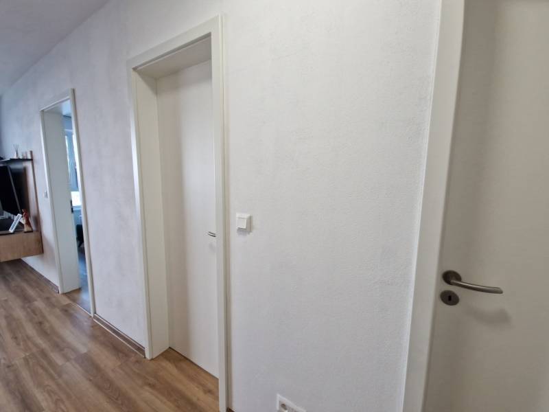 Hallway in a 2-room apartment, white doors and wooden floor, modern furniture in the background.