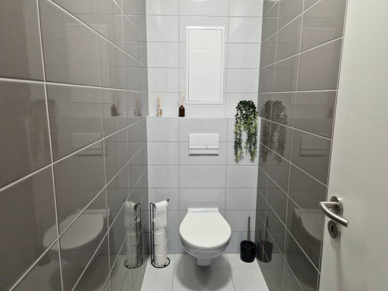Bathroom with a toilet in a 2-room apartment, with dark gray tiles on the walls.