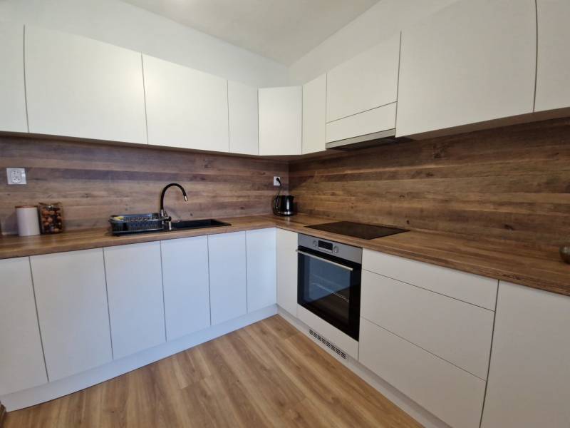 White kitchen in a 2-room apartment with a wooden countertop and floor.