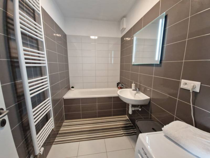 Bathroom in a 2-room apartment with a bathtub, sink, mirror, and ladder radiator.