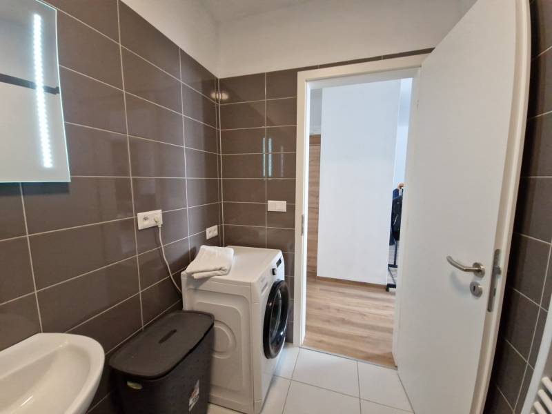Bathroom with a mirror, sink, washing machine, and laundry basket in a 2-room apartment.