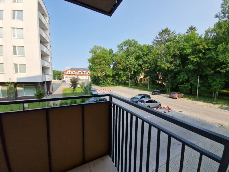 View from the balcony onto Sadová Street in Senica, overlooking the parking lot and greenery.