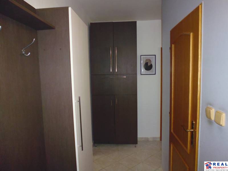 A hallway in a 3-room apartment with dark furniture, white walls, and wooden doors.