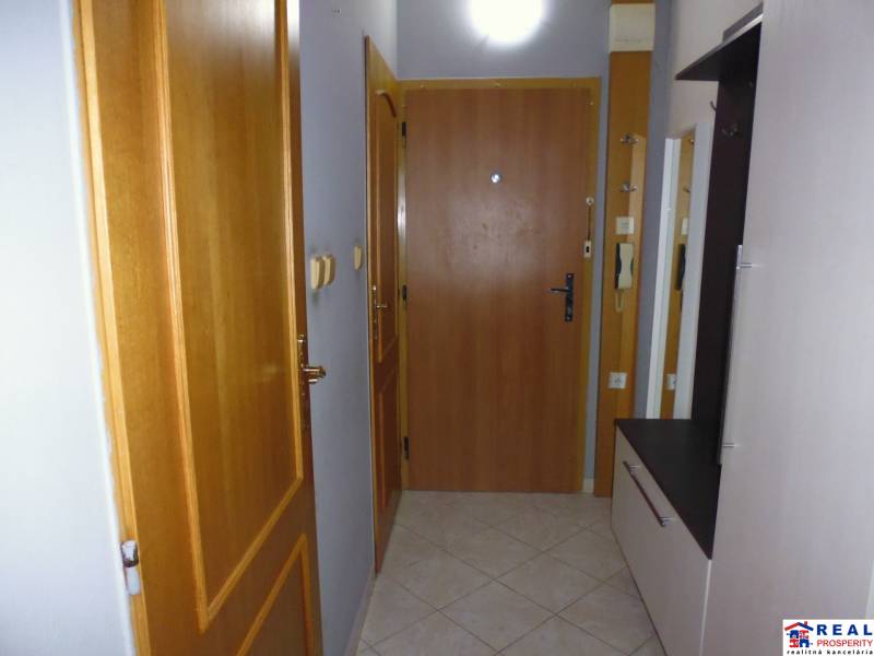 Hallway of a 3-room apartment with wooden doors, a coat rack, and tiled flooring.