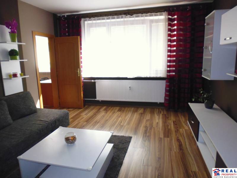 Living room in a three-room apartment with a sofa, table, and curtains on the window.