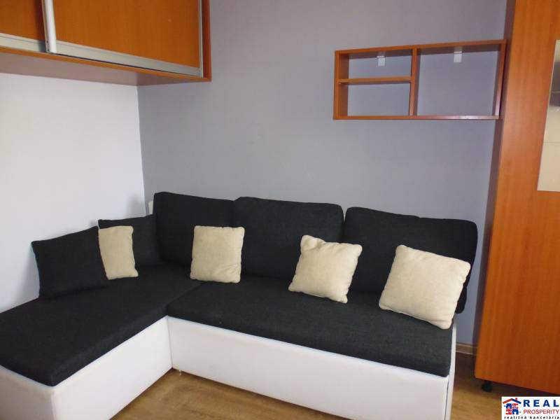 A sofa with cushions in a 3-room apartment, a wall with cabinets and a shelf.