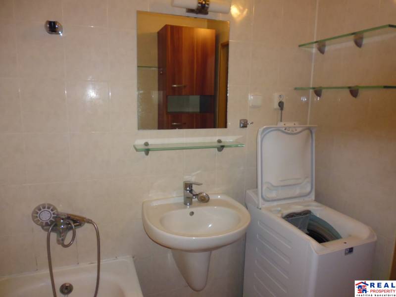 A bathroom in a 3-room apartment with a bathtub, sink, and washing machine, complemented by shelves.