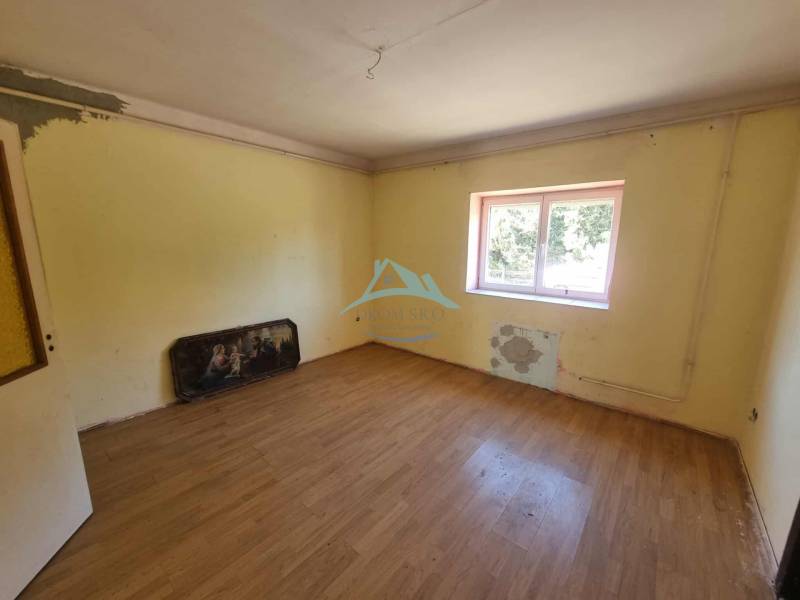 A room in a family house with a wooden floor, a simple ceiling, and a window facing the yard.