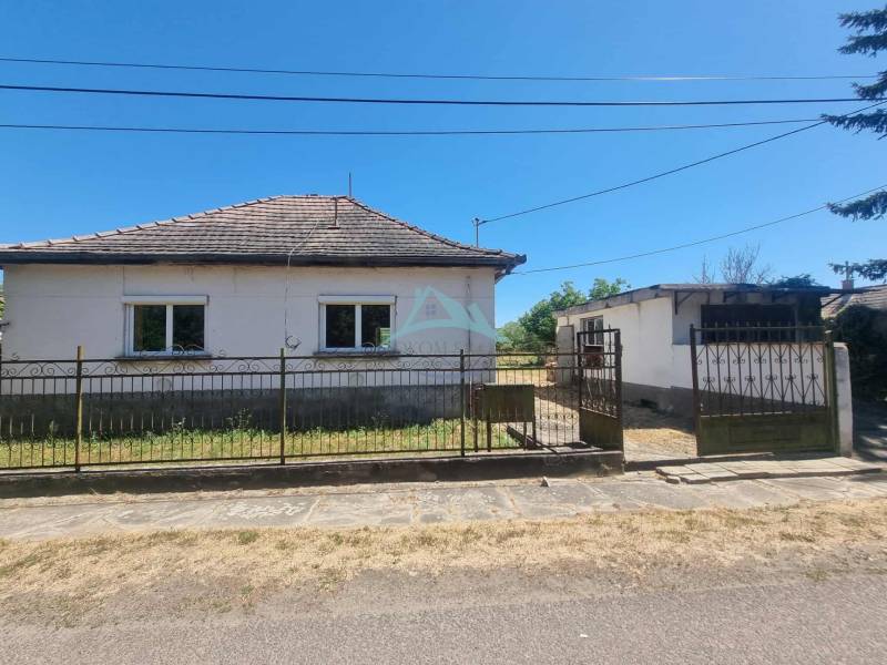 A family house in Ipolyvec with a fence, garage, and garden, the sky is clear.