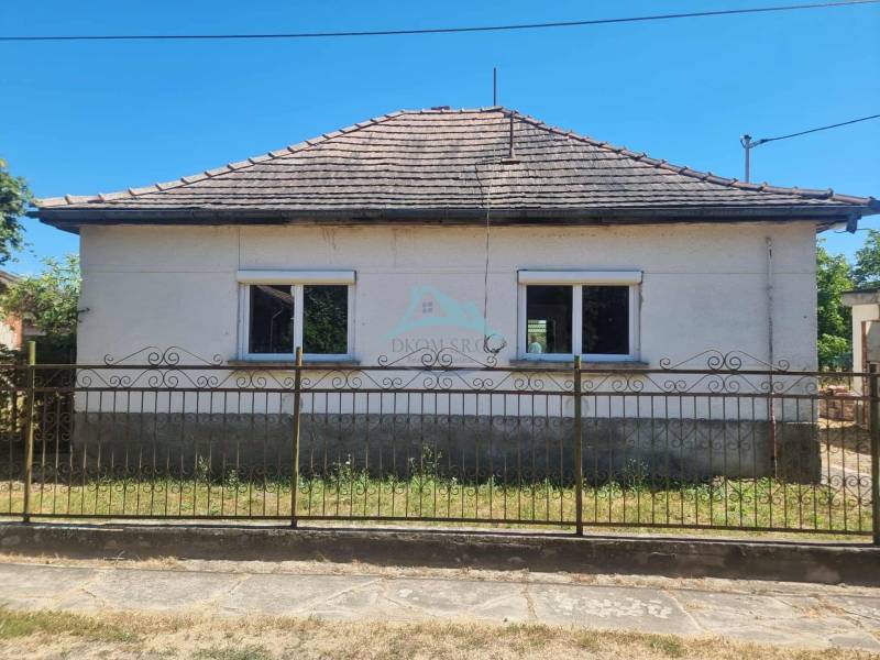 A family house in Ipolyvec with two windows and a sloping roof behind a metal fence.