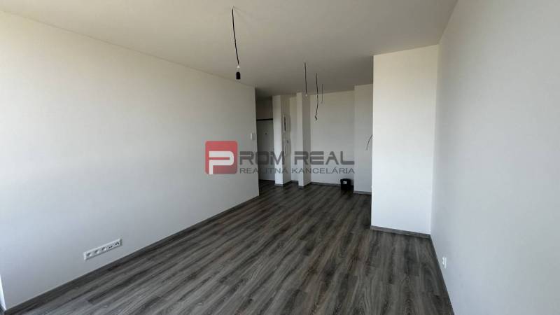 An empty living room in a two-room apartment with laminate flooring and bare walls.