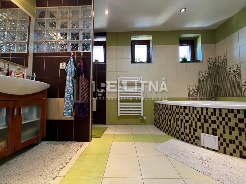 A bathroom with a bathtub and a sink in a family house, with tiles combining green and brown colors.