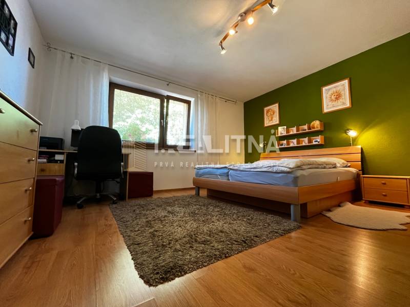 Bedroom in a family house with a wooden bed, green wall, and a work corner.
