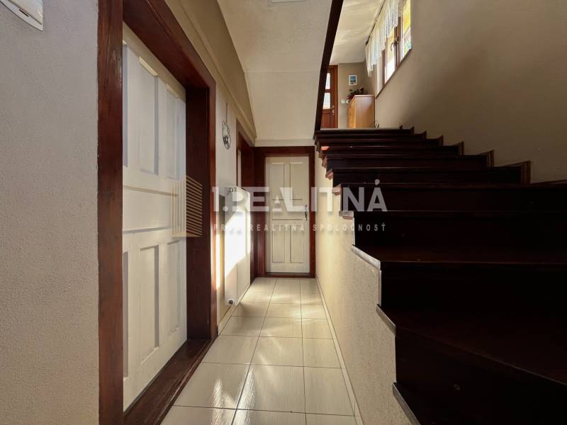 A hallway with a staircase and wooden details in a family house, entrance to a room with white doors.