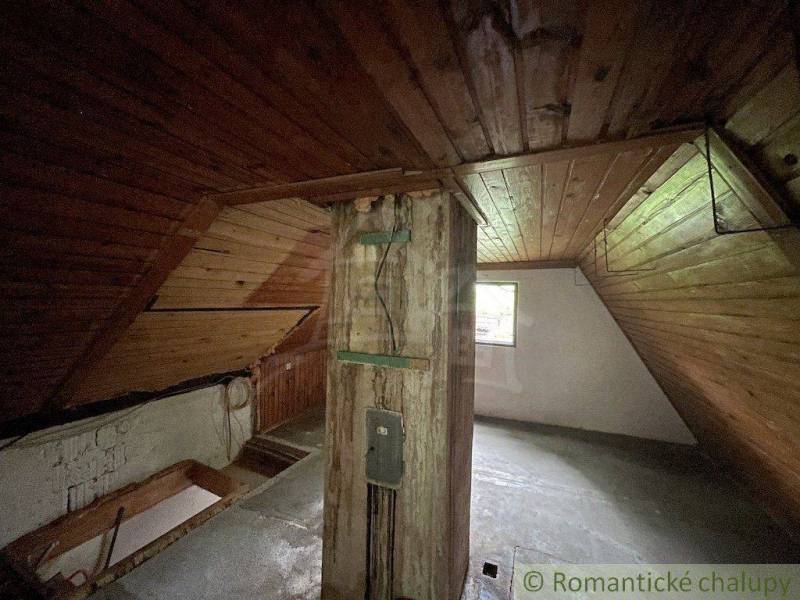 Attic in a family house with wooden paneling and a beam, illuminated by a window.
