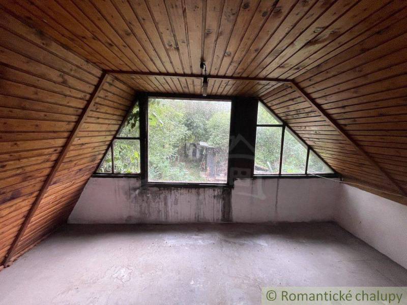 Attic room with wooden paneling and a view of the garden in a family house.