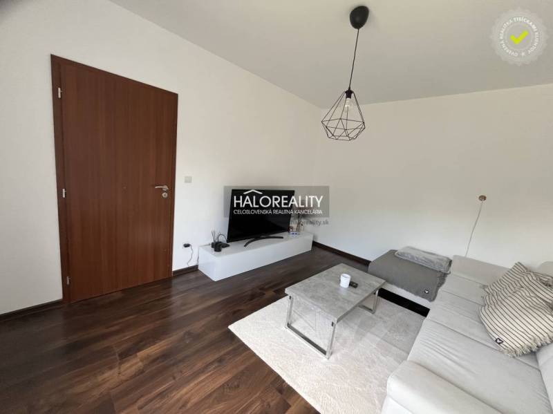 A living room in a family house with a dark floor, a white sofa, and a TV stand.