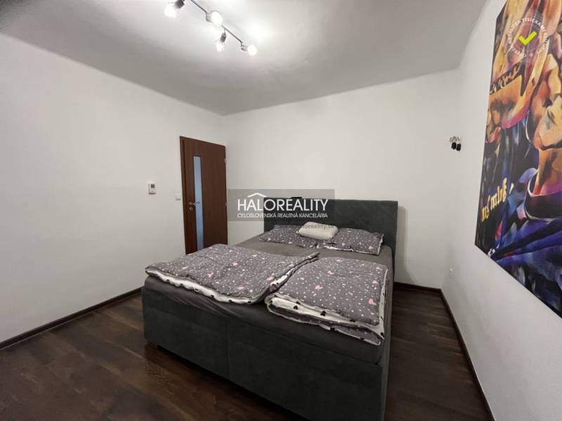 Bedroom in a family house with a bed, dark floor, and a picture on the wall.