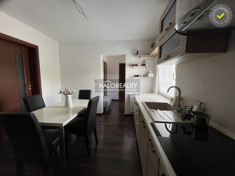 A furnished kitchen and a dining table with black chairs in a family house.