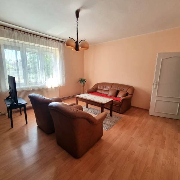 Living room of a family house with a sofa, armchairs, a television, and a wooden table on a carpet.