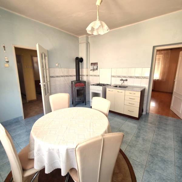 A kitchen in a family house with a table, chairs, a stove, and a tiled stove.